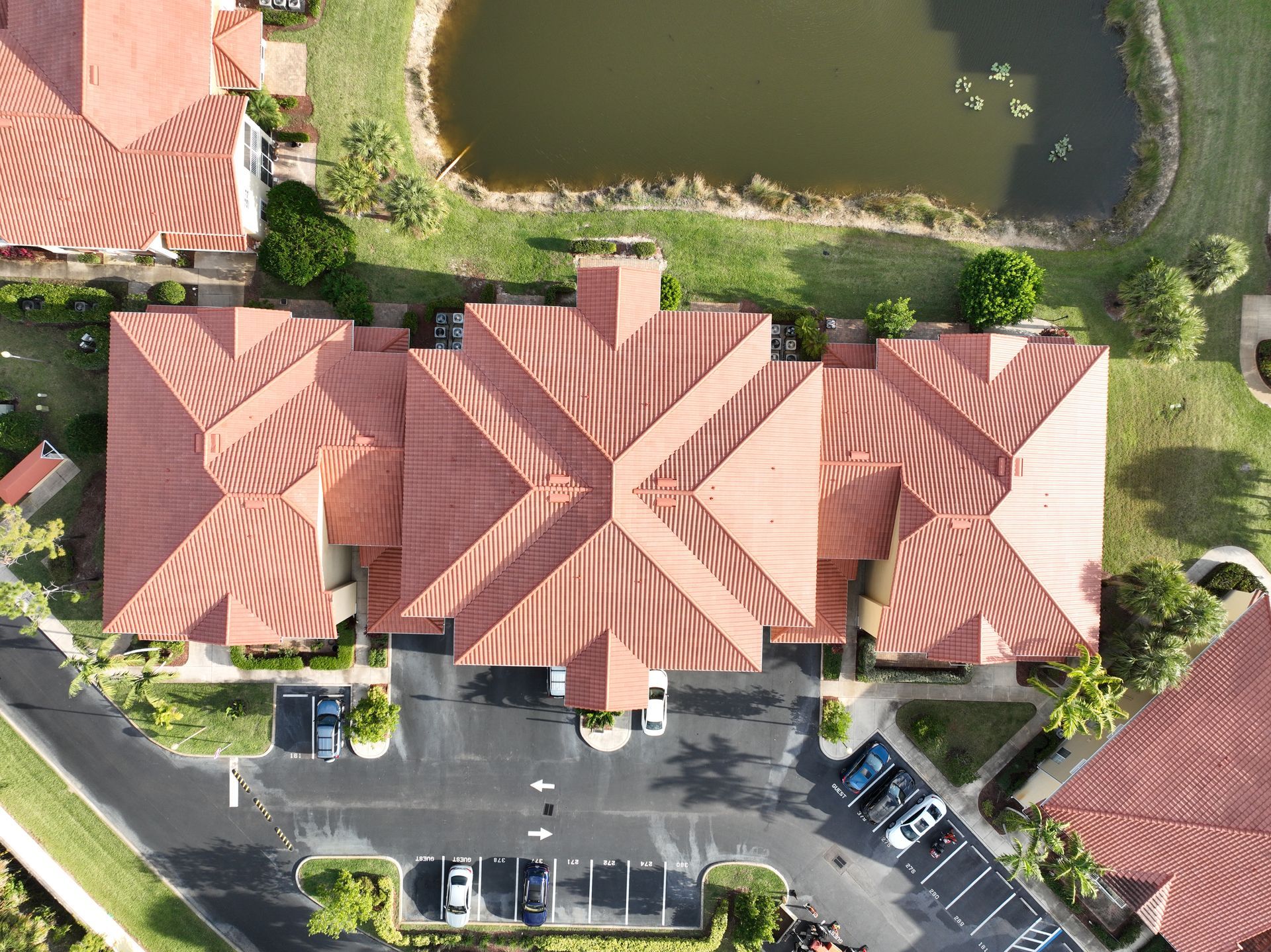 Aerial view of a complex with red tile roofs, parking lot, and a small pond.