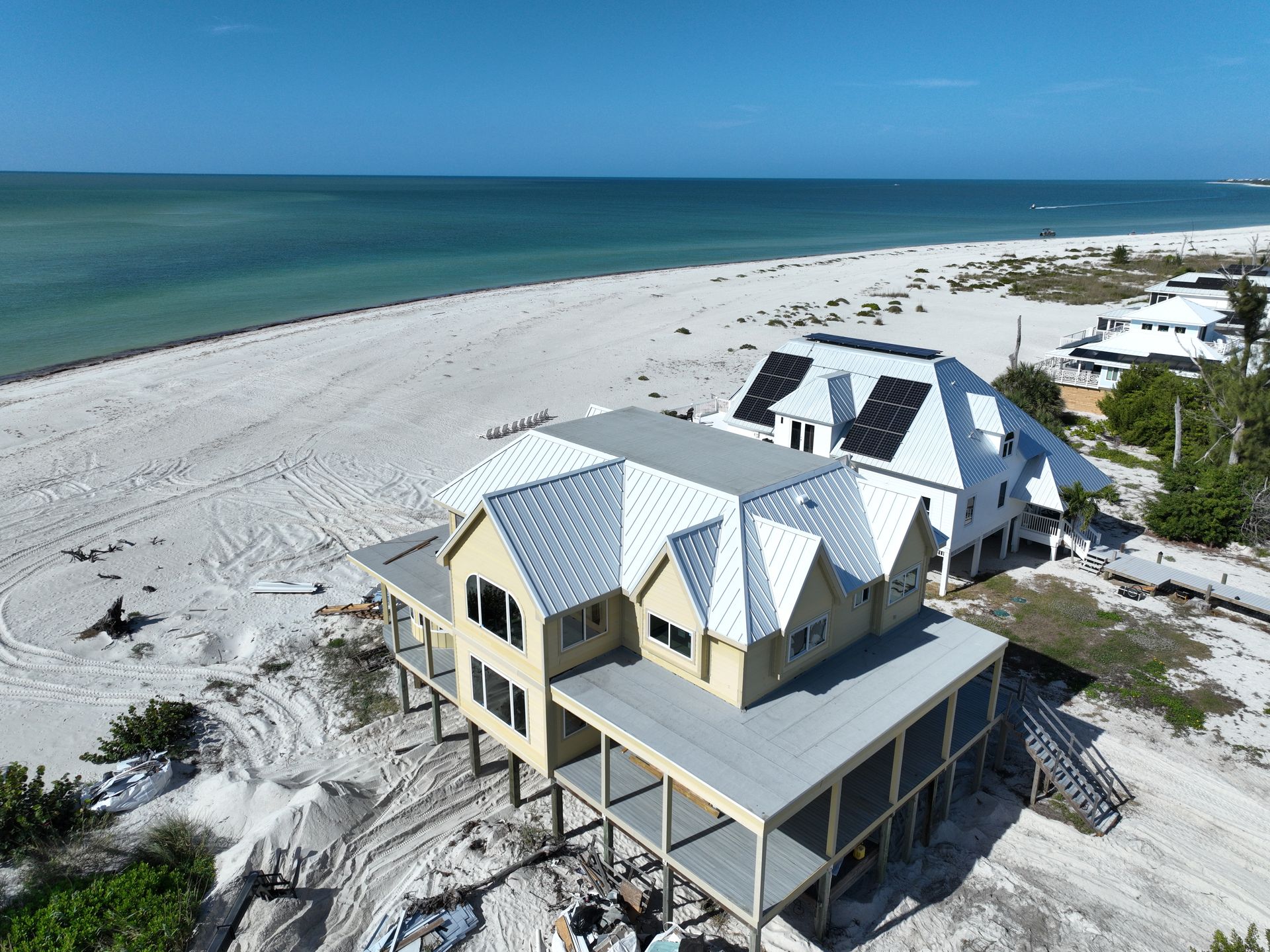 Beachfront homes with metal roofs, light sand, and ocean view.