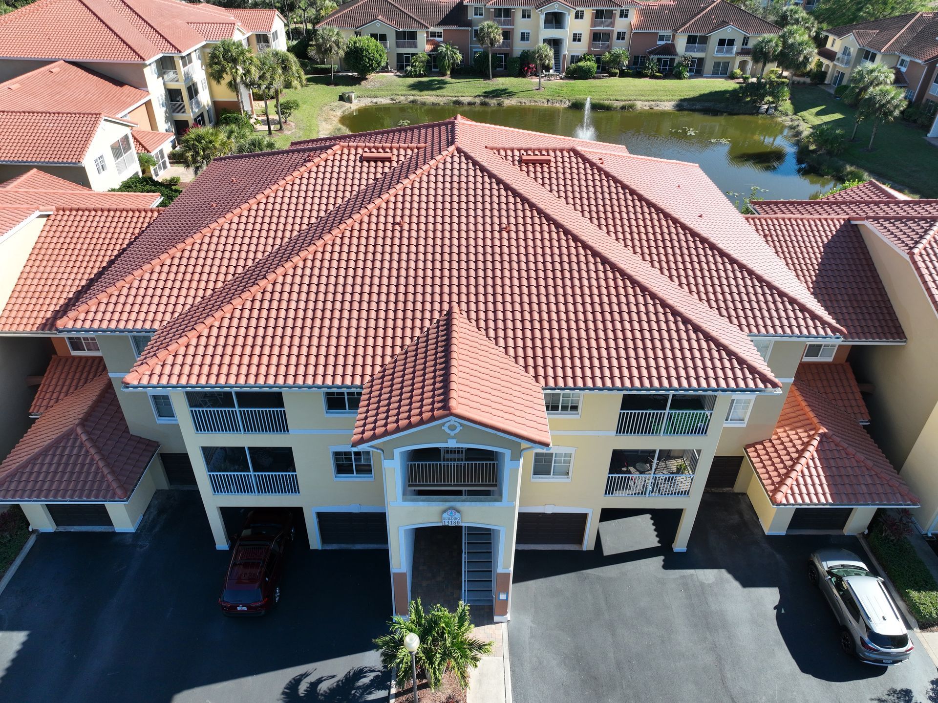 An aerial view of a multi-unit building with a red tile roof and yellow walls, near a pond.