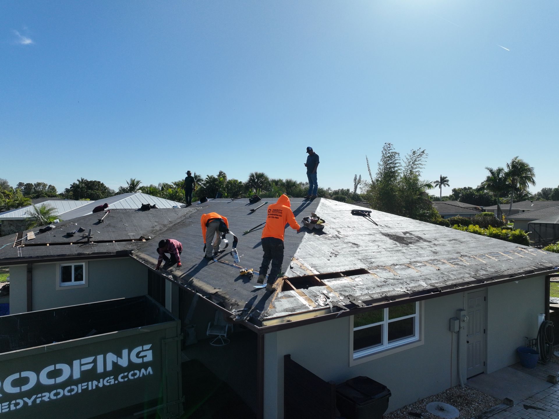 Roofers working on a house roof on a sunny day. They are wearing orange vests.