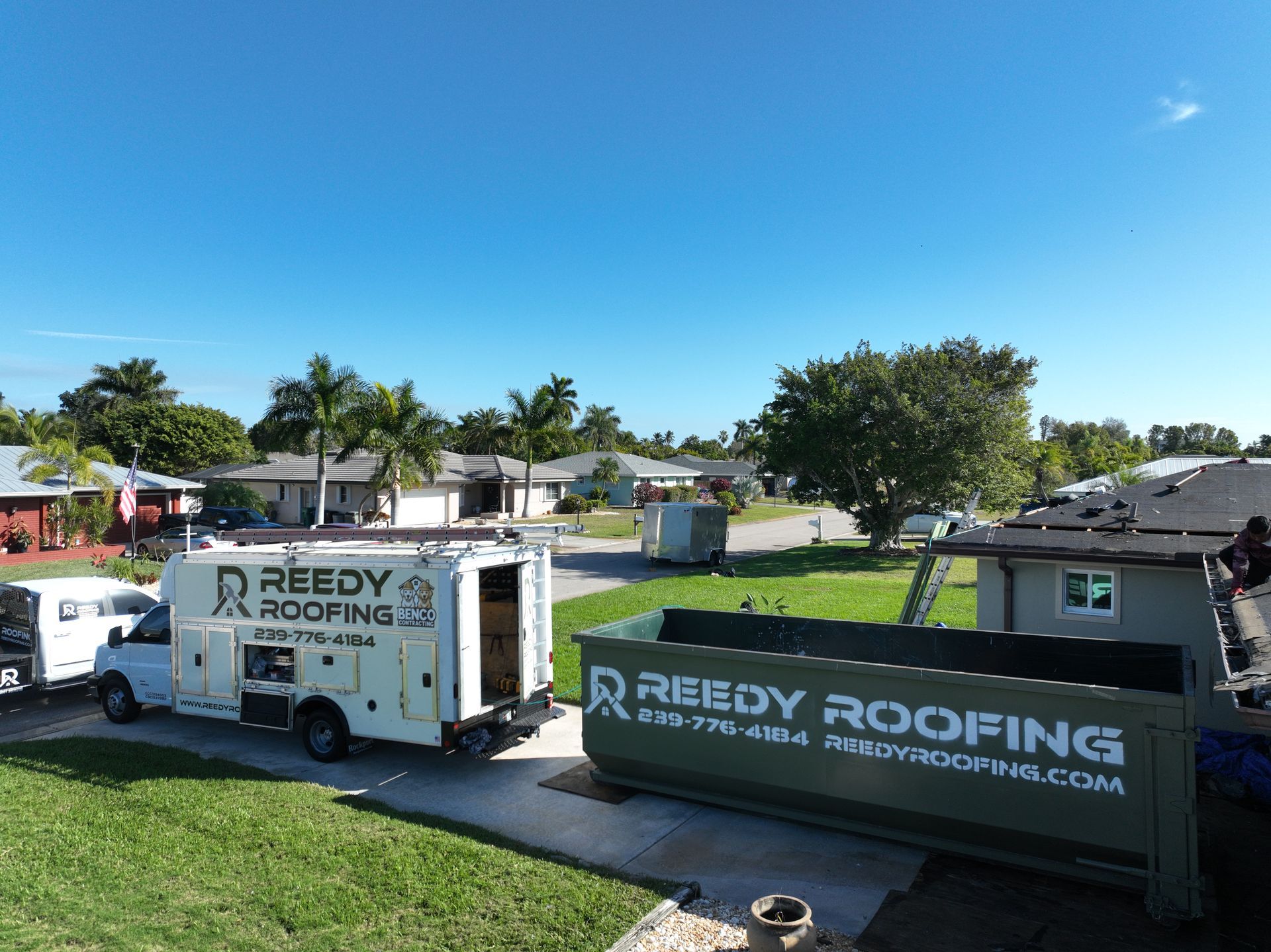 Reedy Roofing truck and dumpster on residential property under a blue sky, preparing for roofing work.