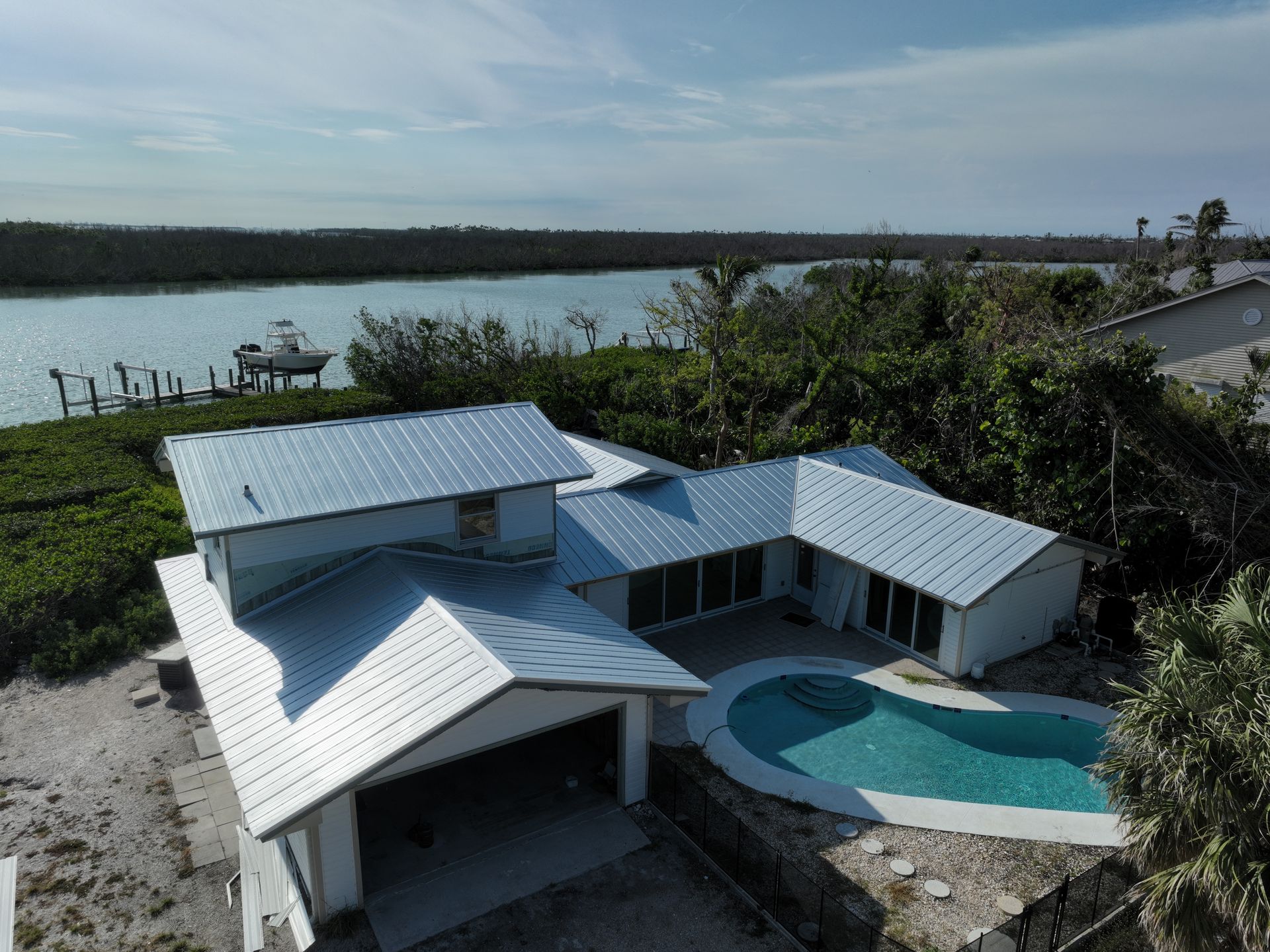 Aerial view of a white house with a pool, metal roof, and dock on the water.