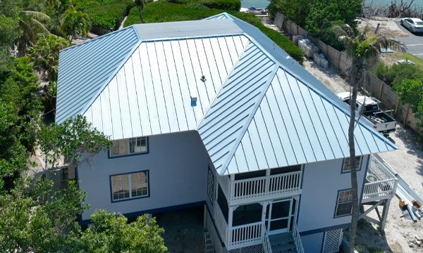 Two-story house with light blue siding and a light blue metal roof. White balconies and green trees surround the home.