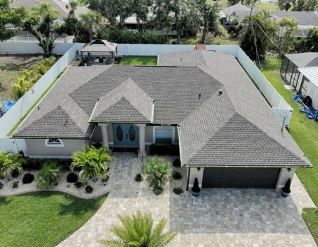 Aerial view of a suburban house with a gray roof, surrounded by a white fence and a green lawn.