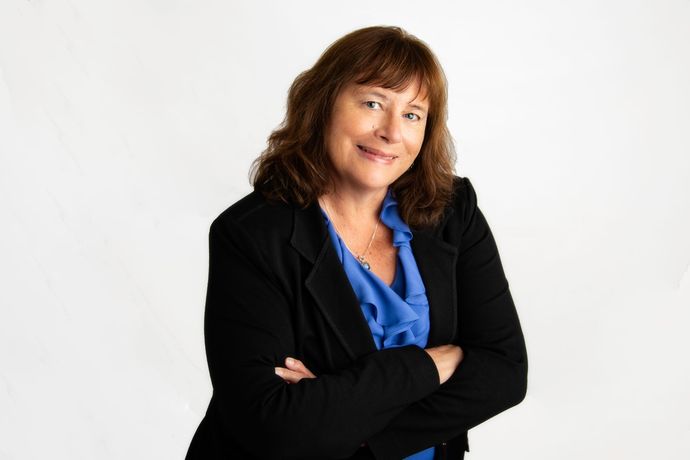 A woman in a black jacket and blue shirt is standing with her arms crossed.