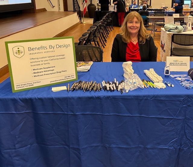 A woman sits at a table with a sign that says benefits by design