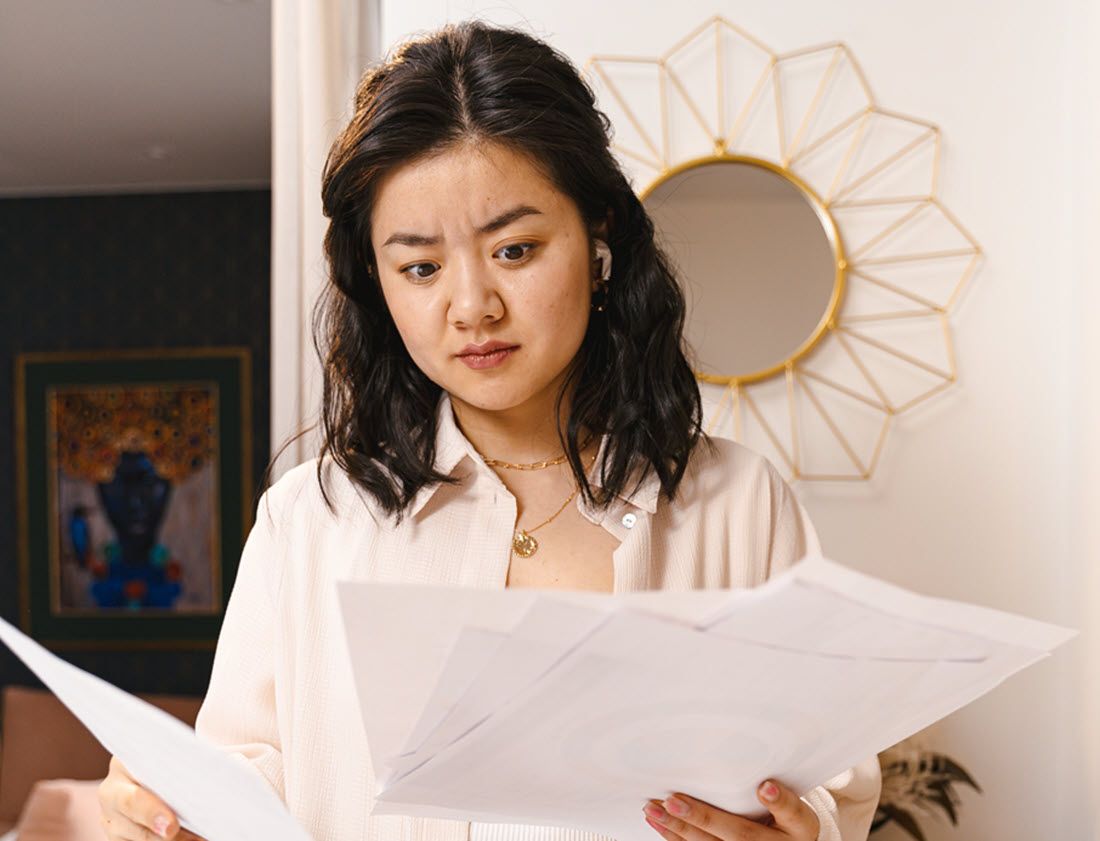 Woman in a white blouse reviewing several papers, looking confused.