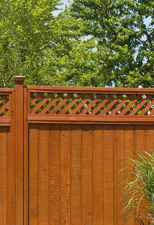 Wooden fence with lattice top, stained brown, trees in the background.