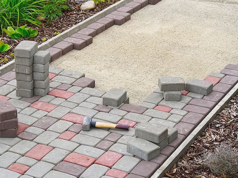 Path construction: bricks in progress, alternating red/gray, hammer visible, outdoor setting.
