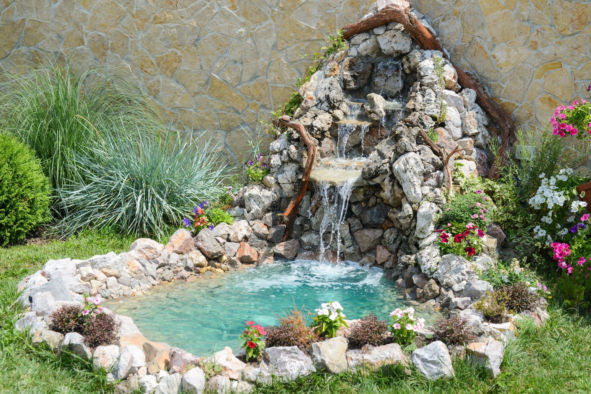 Small backyard waterfall feature with turquoise water and stone work, surrounded by plants.