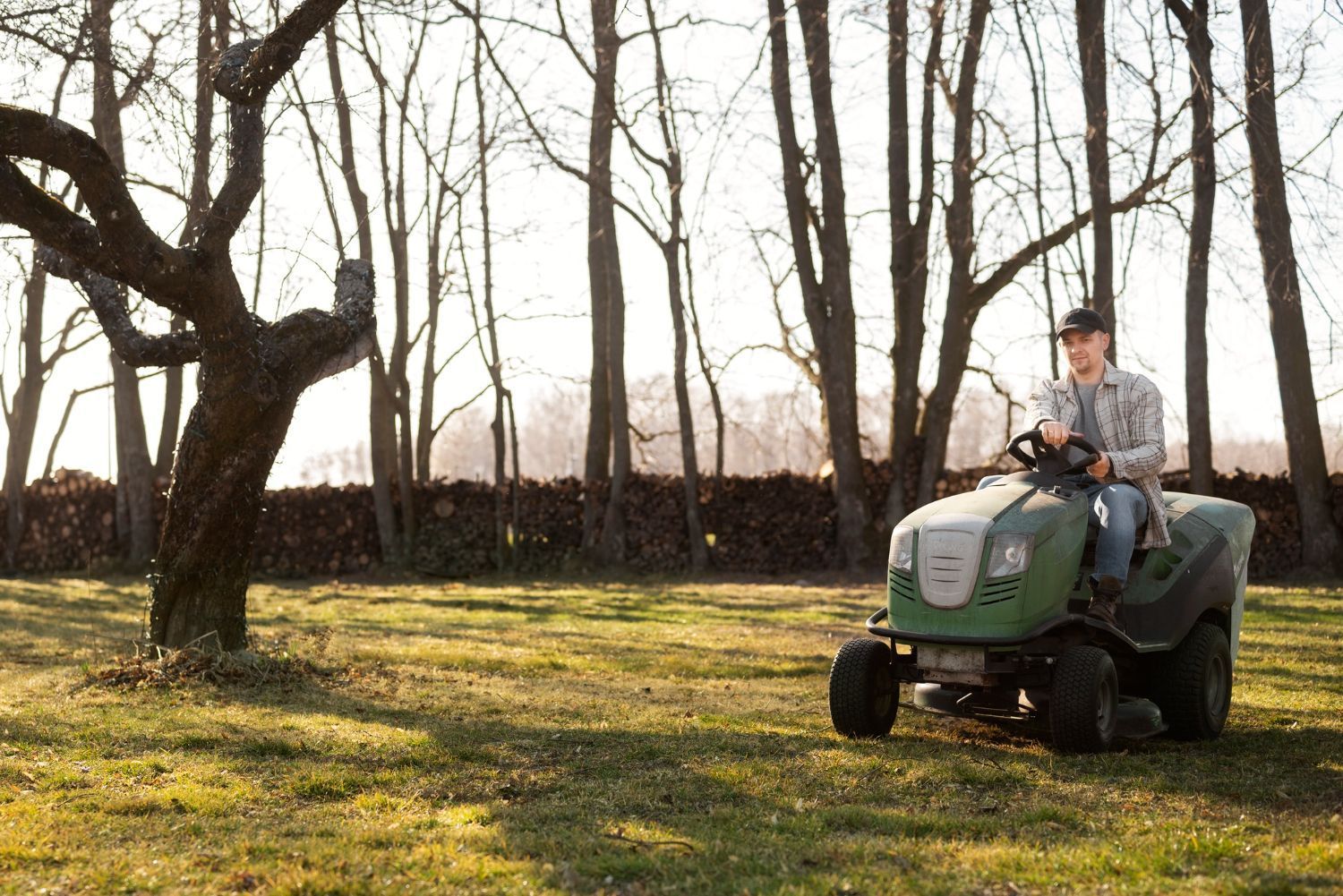Man on a green riding lawnmower mowing a grassy yard, trees in background.