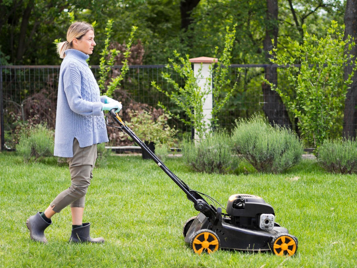 Woman mowing a green lawn with a black and orange mower in a backyard.