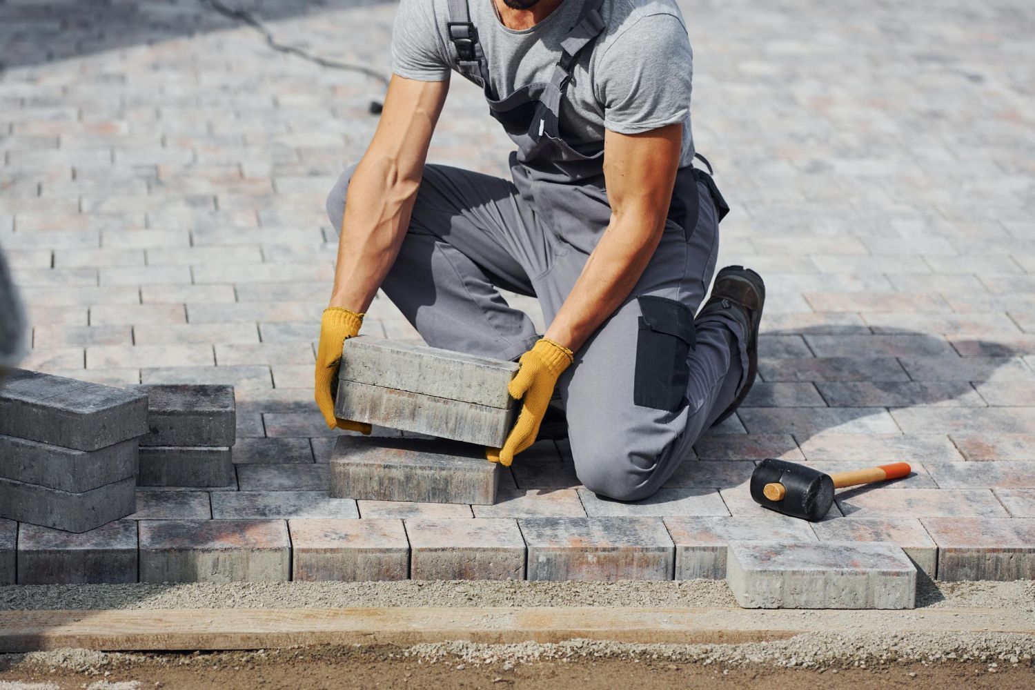 Man laying grey paving stones, wearing gloves, in an outdoor setting.
