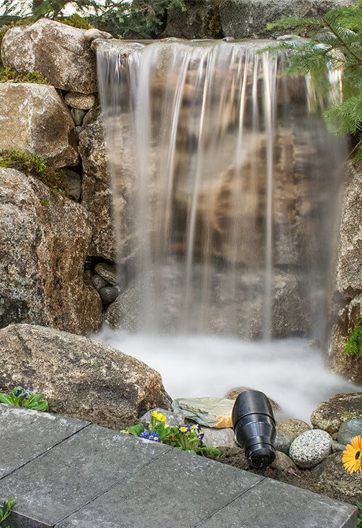 Waterfall cascading over rocky stones. Water is blurry. A spotlight is in the foreground.