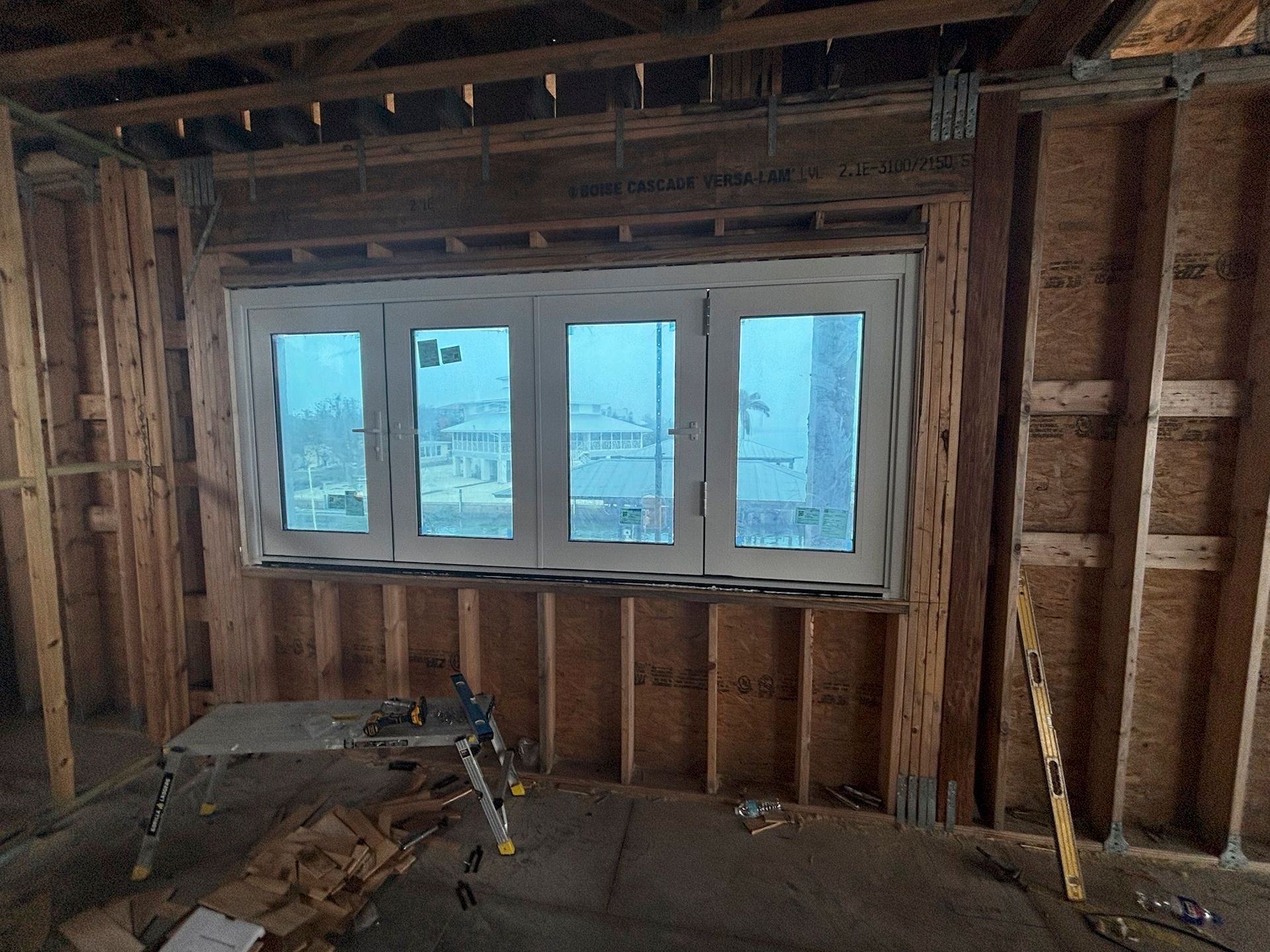 Interior view of a building under construction, featuring a large window. Unfinished wooden walls and framing.