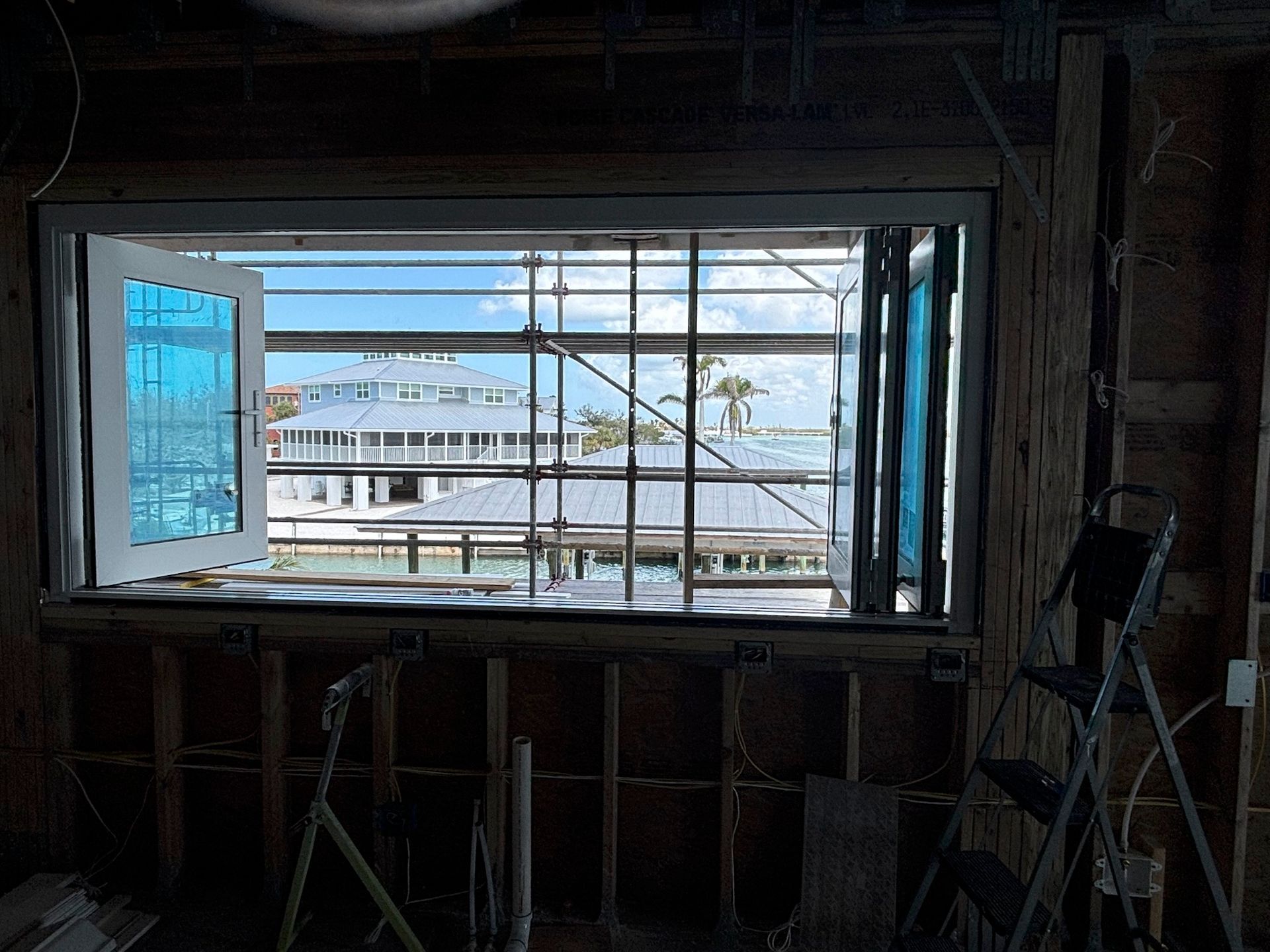 Interior view of a building under renovation with a window overlooking a waterfront and partial blue-tinted window panes.