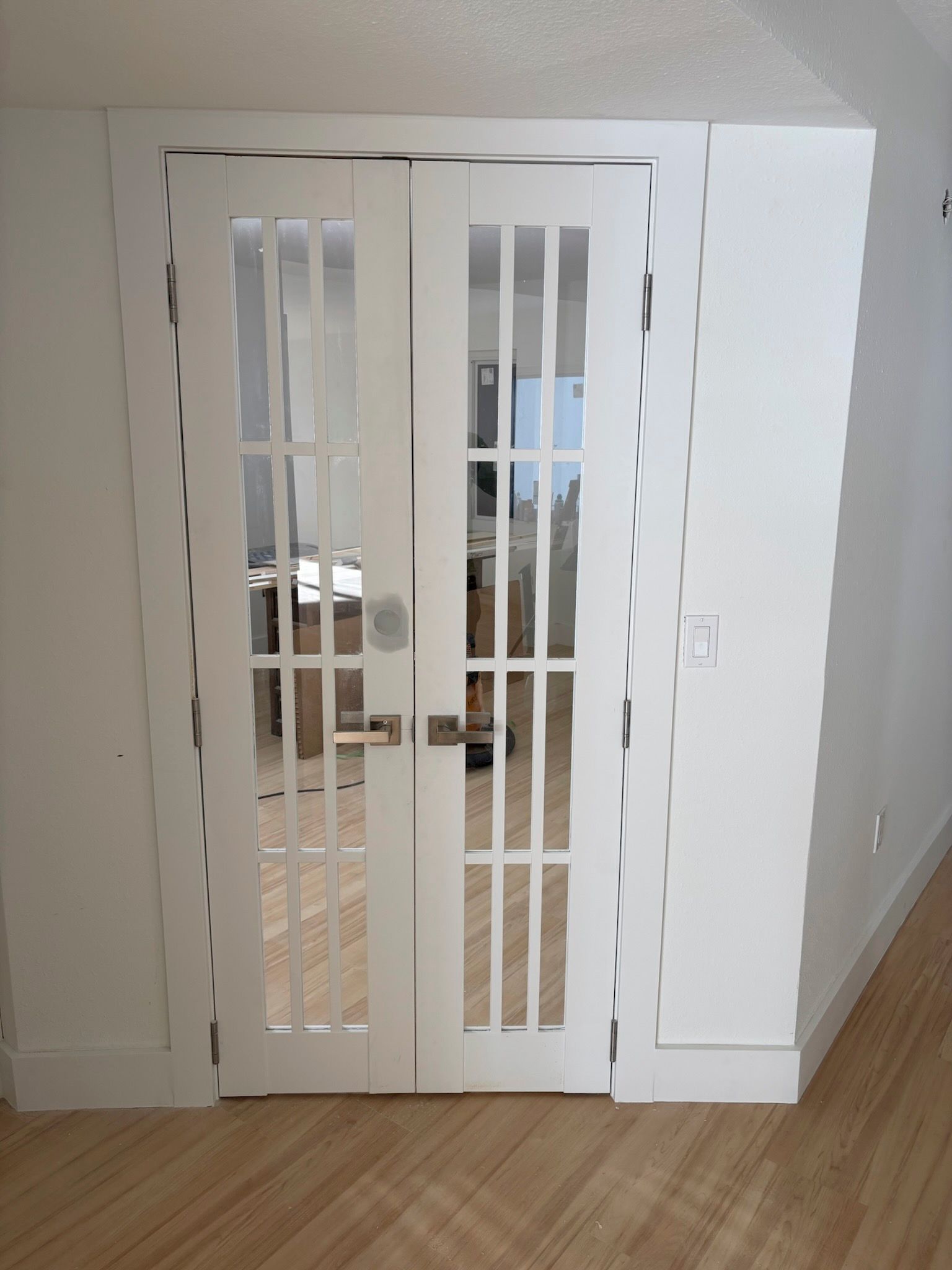 Double white doors with glass panes, set in a white doorway. The doors are slightly ajar, revealing a room with a desk.