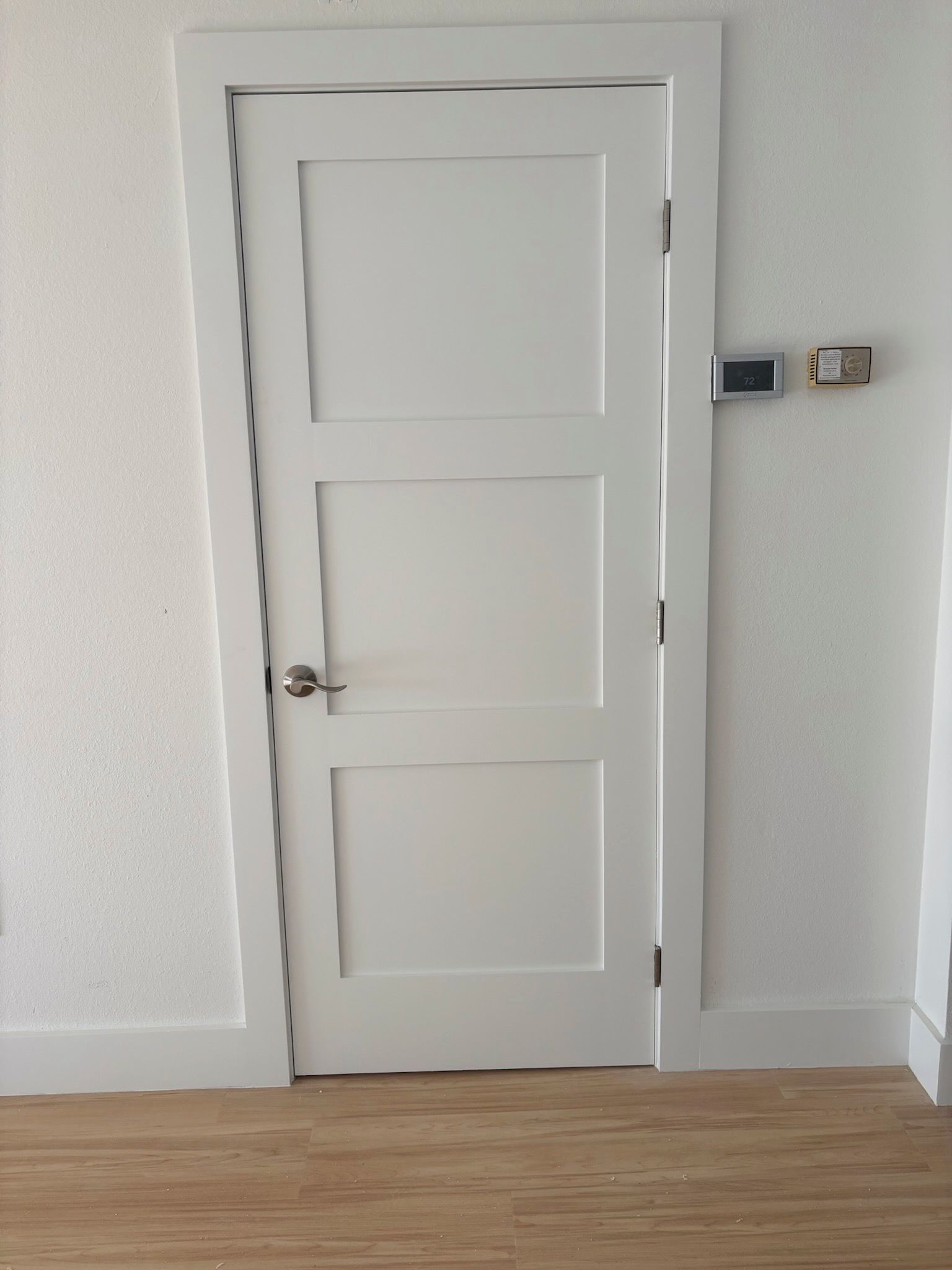 White three-panel interior door with silver handle and frame, set in white wall.
