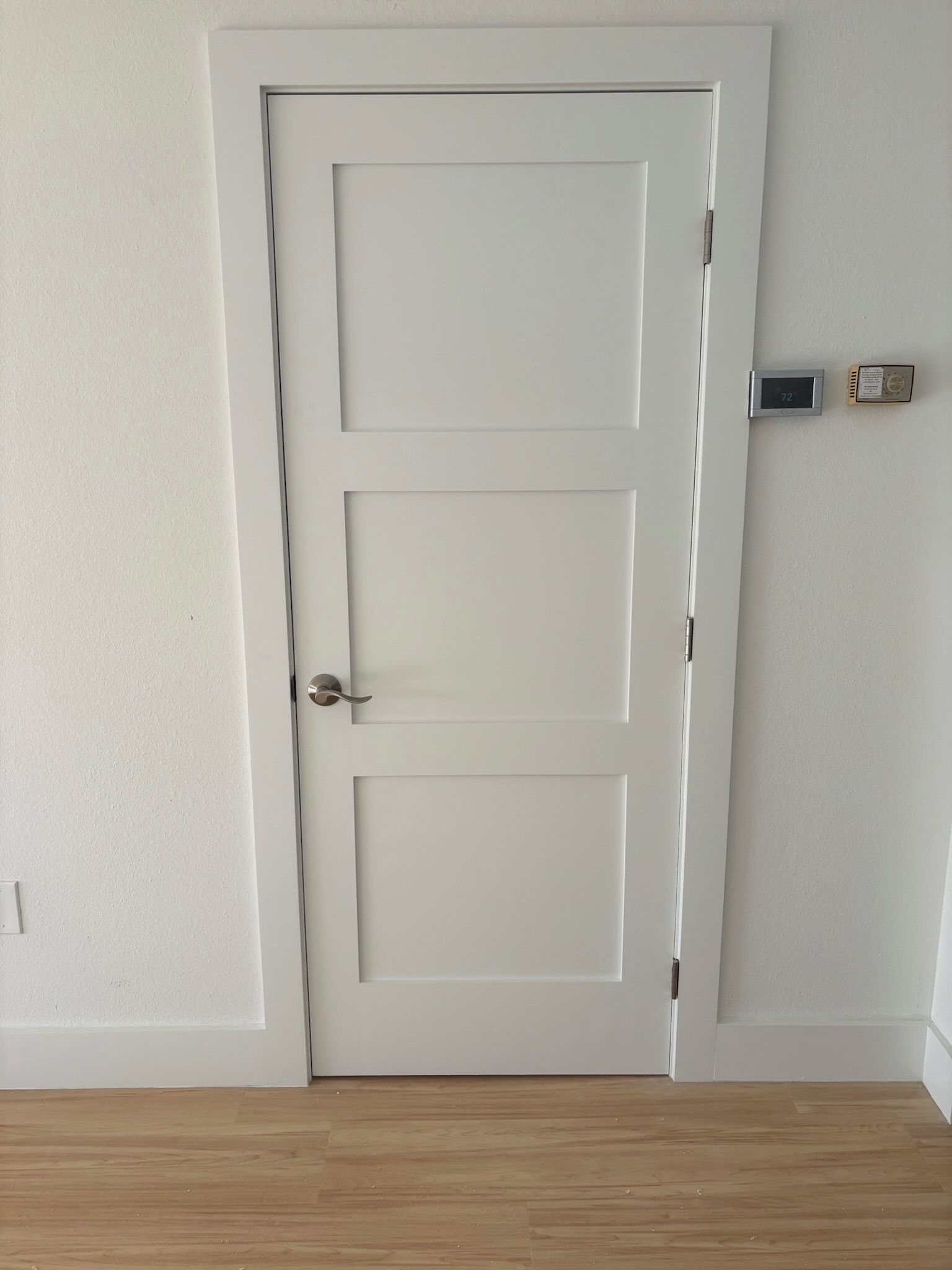 White three-panel interior door with white trim and a silver handle, set in a white wall with wooden flooring.