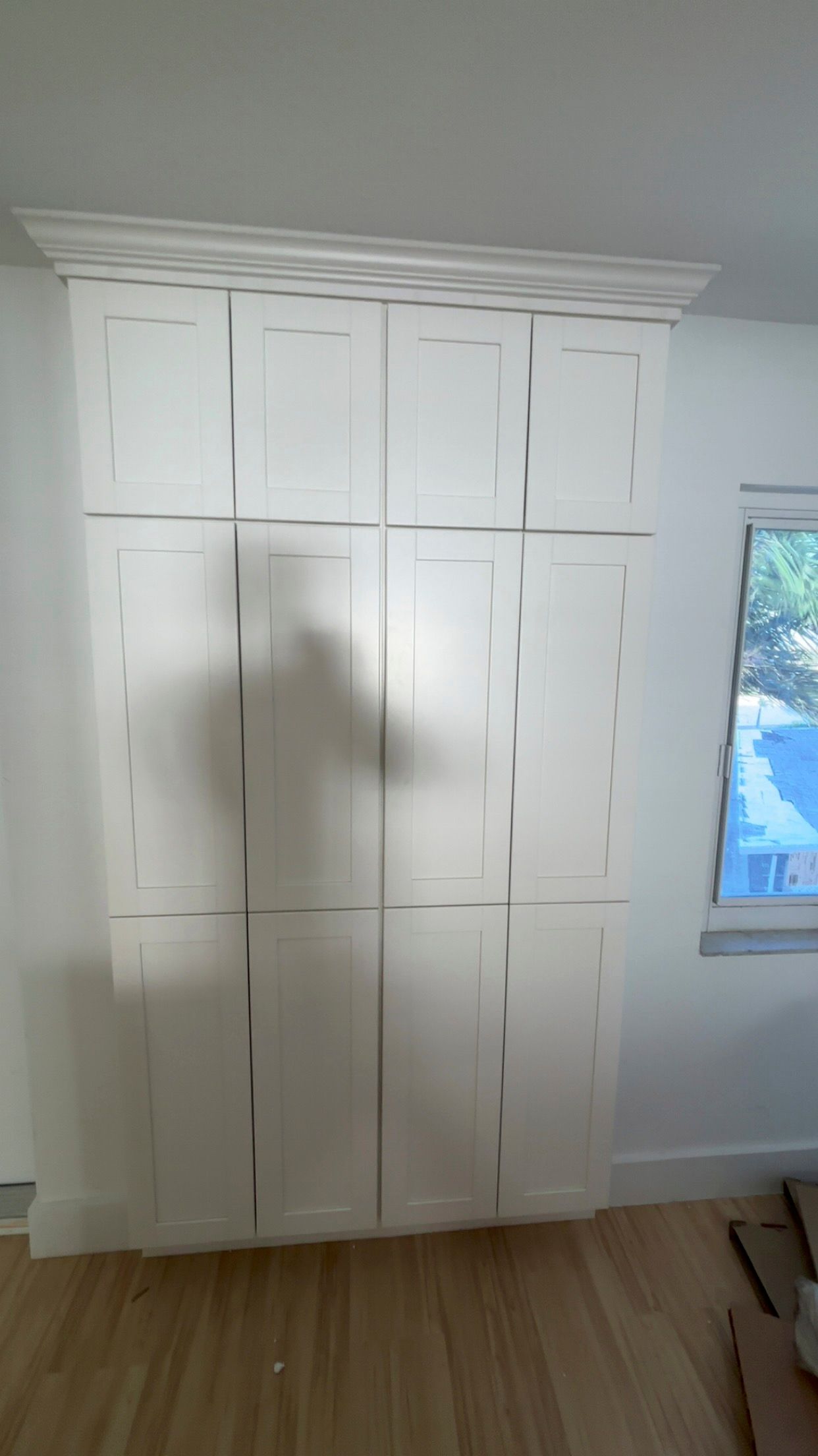 White cabinets filling a wall, topped with decorative molding. Shadow of a person is visible.