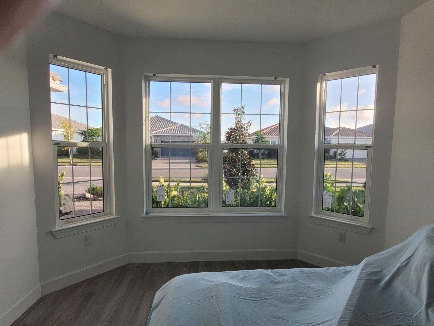 Bedroom with bay windows overlooking a street. Blue sky and houses are visible.