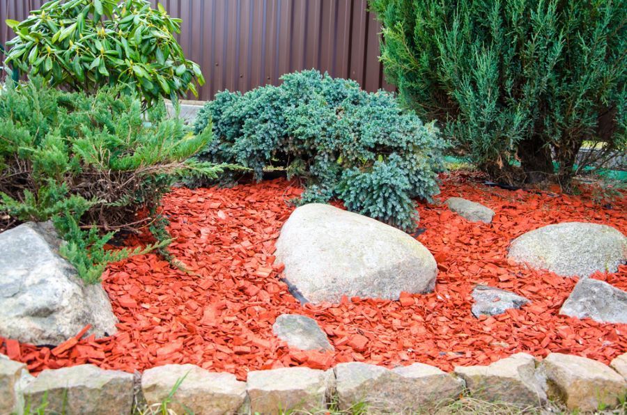A Garden Filled with Rocks, Plants and Red Mulch — Troy Weier Tree Service In Frenchville, QLD