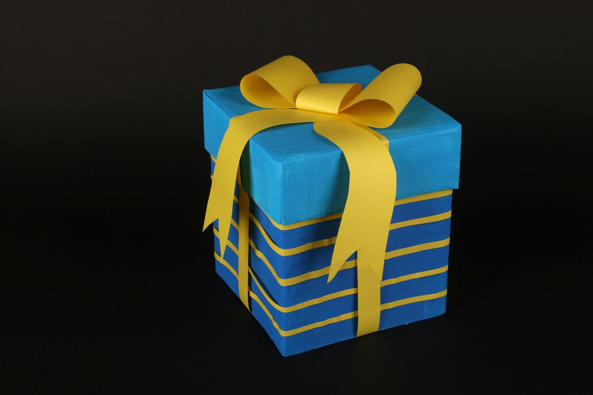 Blue gift box with yellow ribbon against a black background.