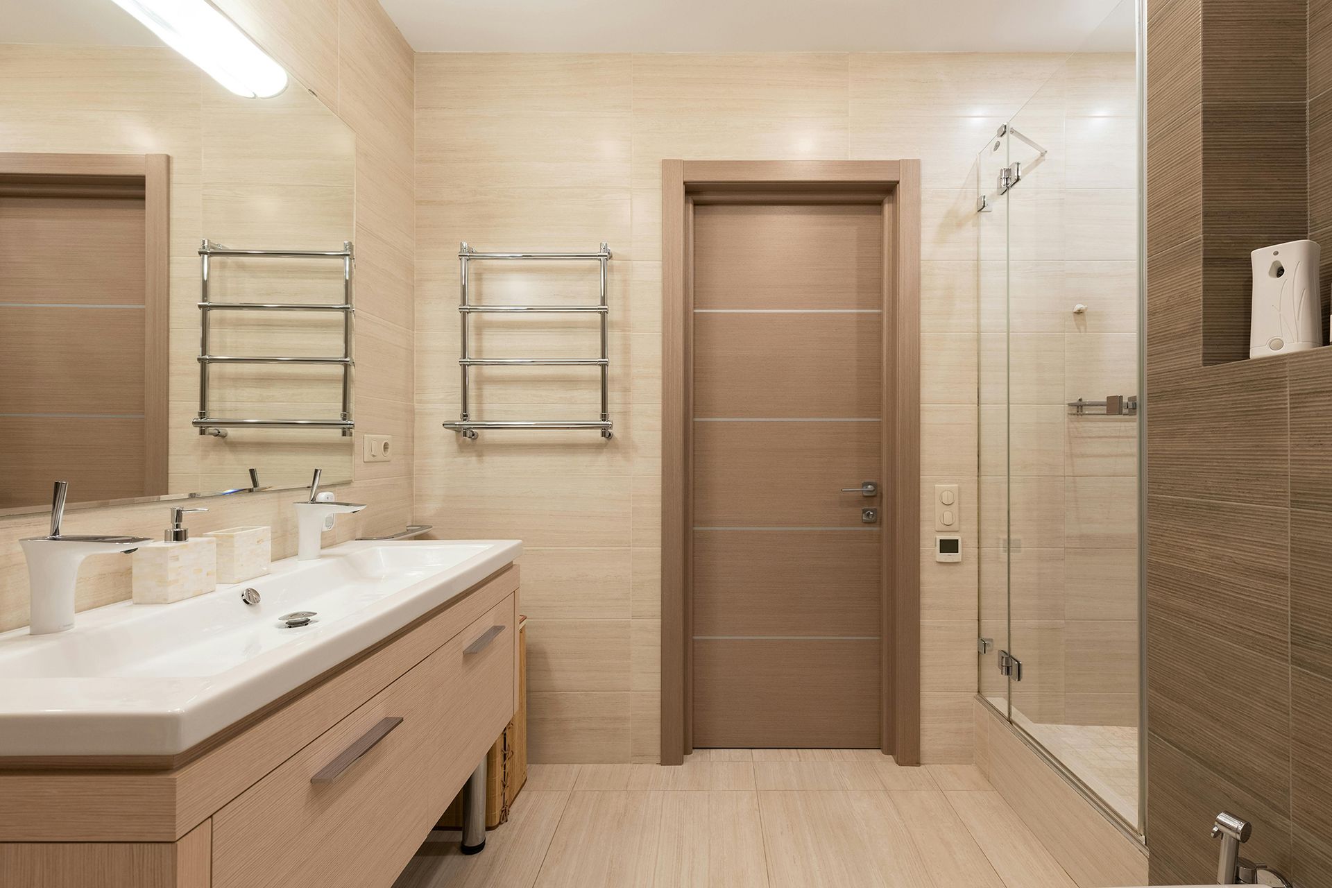 Bathroom with light wood cabinets, beige tile walls, and a glass shower.