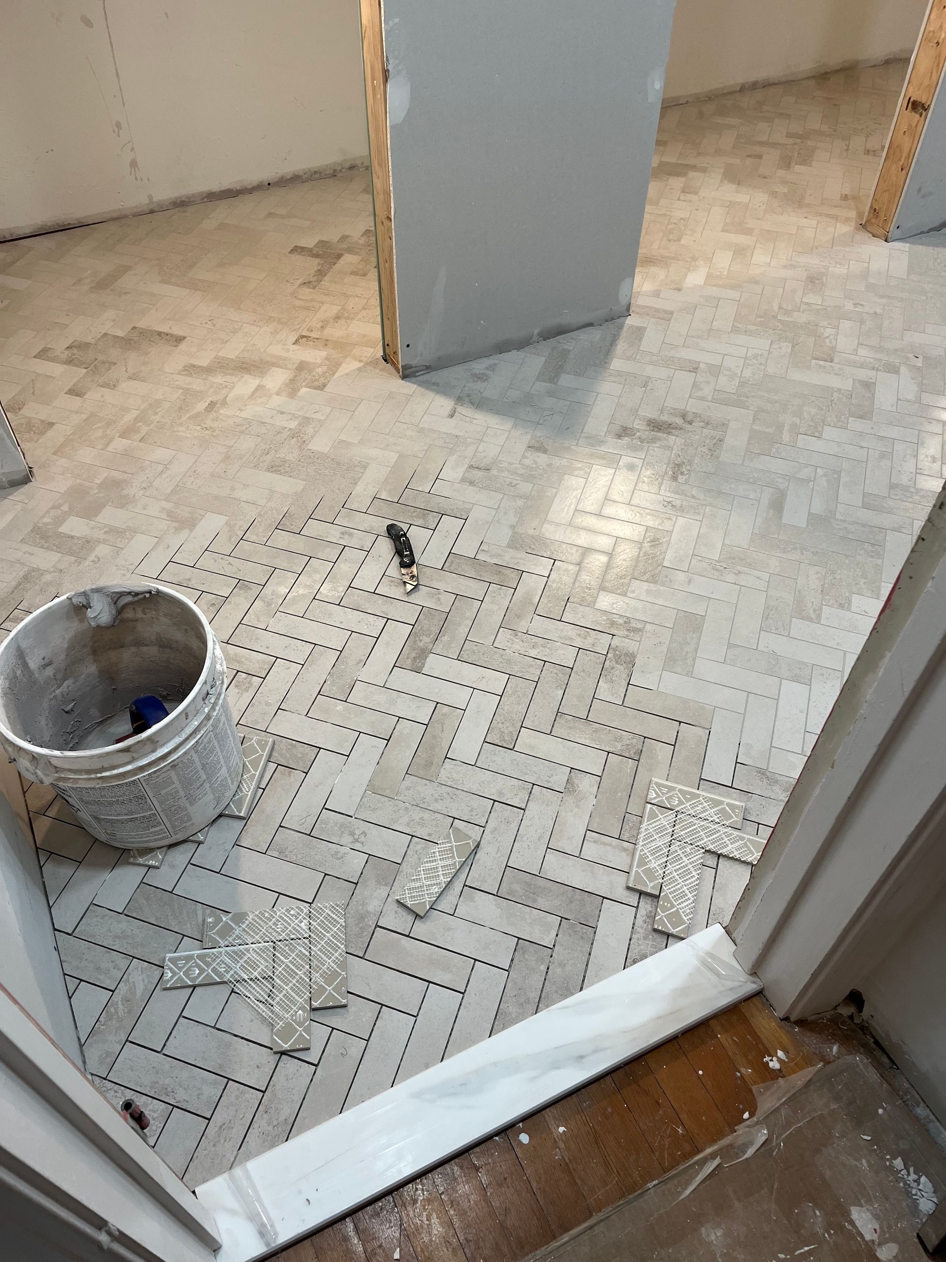 Basement floor with herringbone tile pattern, bucket, and construction debris.