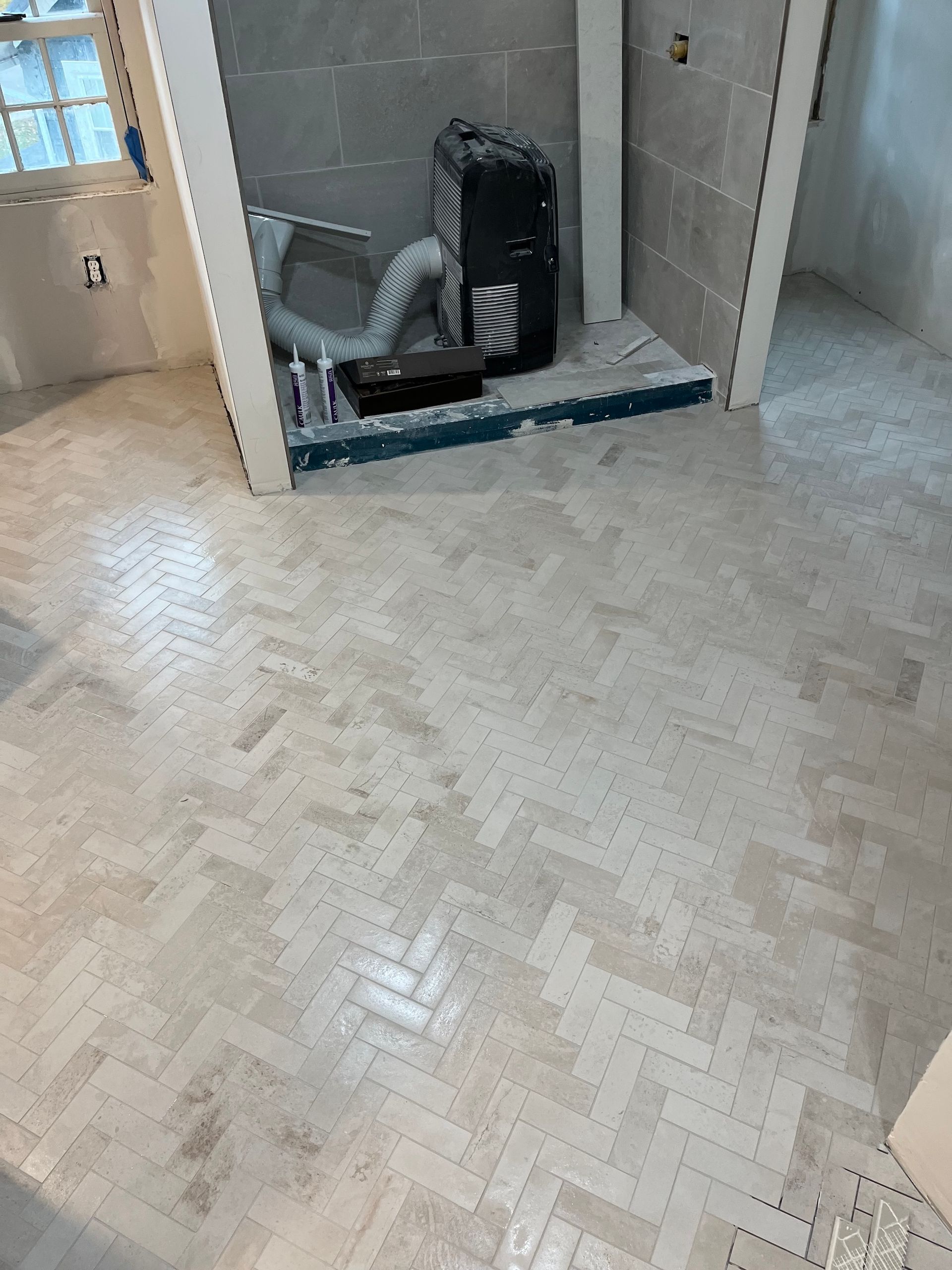 Herringbone tile floor in a bathroom under construction, with gray shower tile and tools.