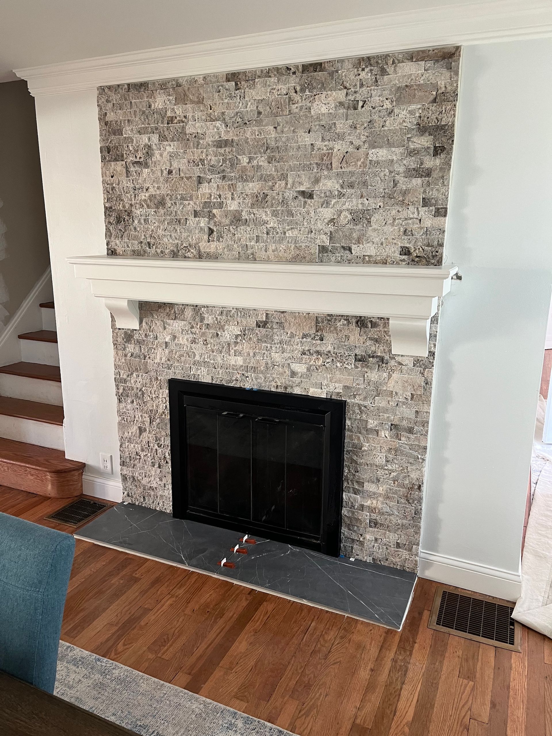 Fireplace with stone tile surround, white mantel, black firebox, and gray hearth.