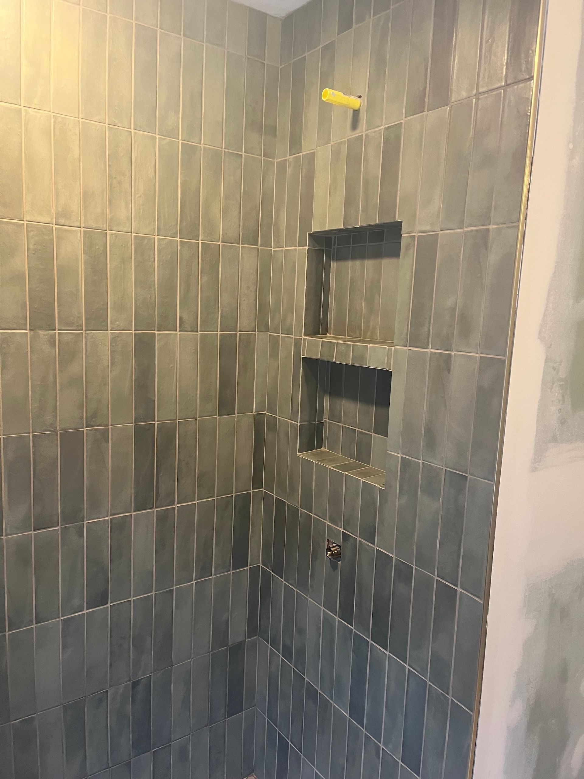 Shower with gray vertical tiles and built-in shelves. Yellow shower head.