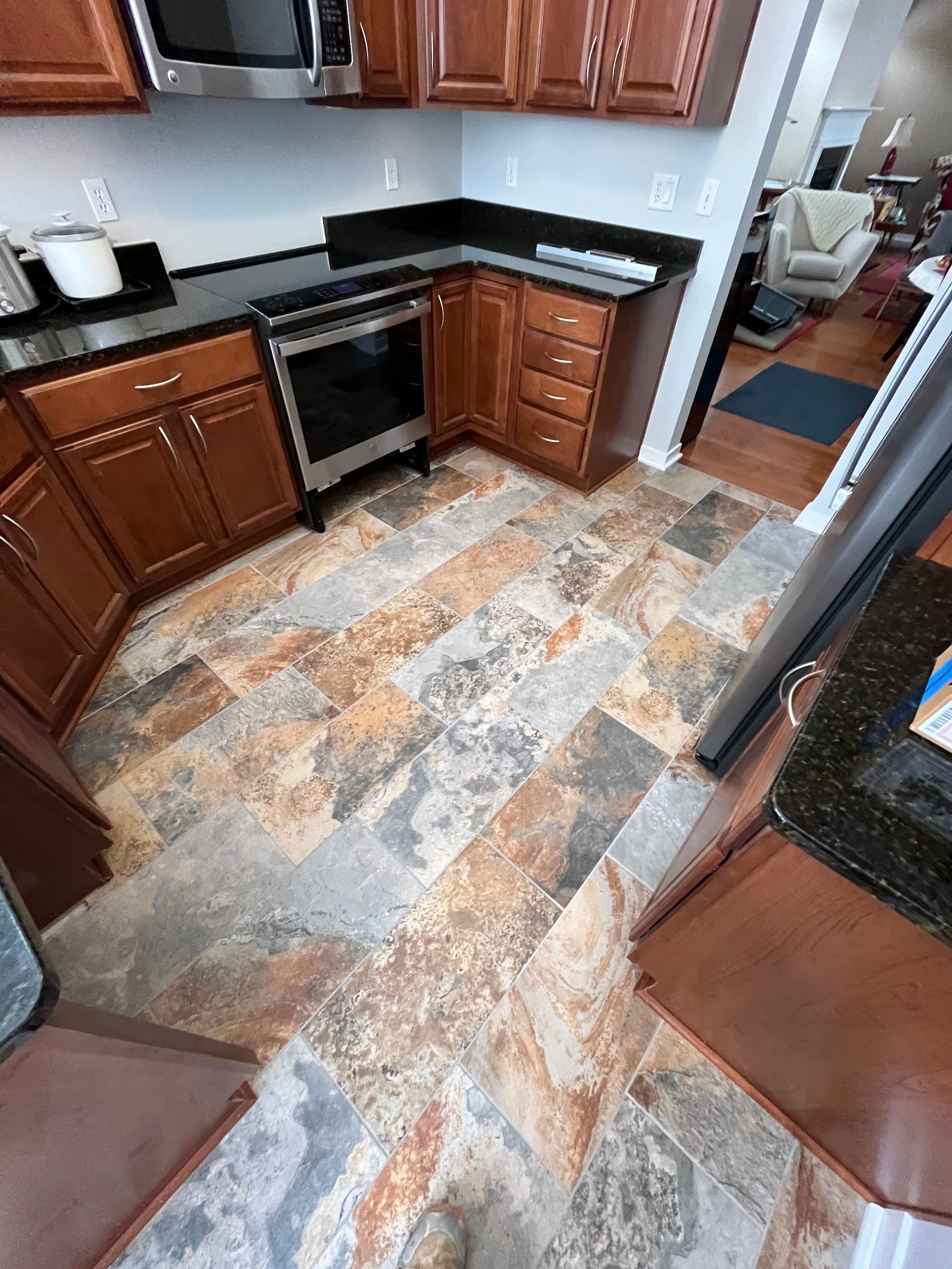 Kitchen with brown cabinets, black countertops, and patterned tile flooring. Stainless steel oven.