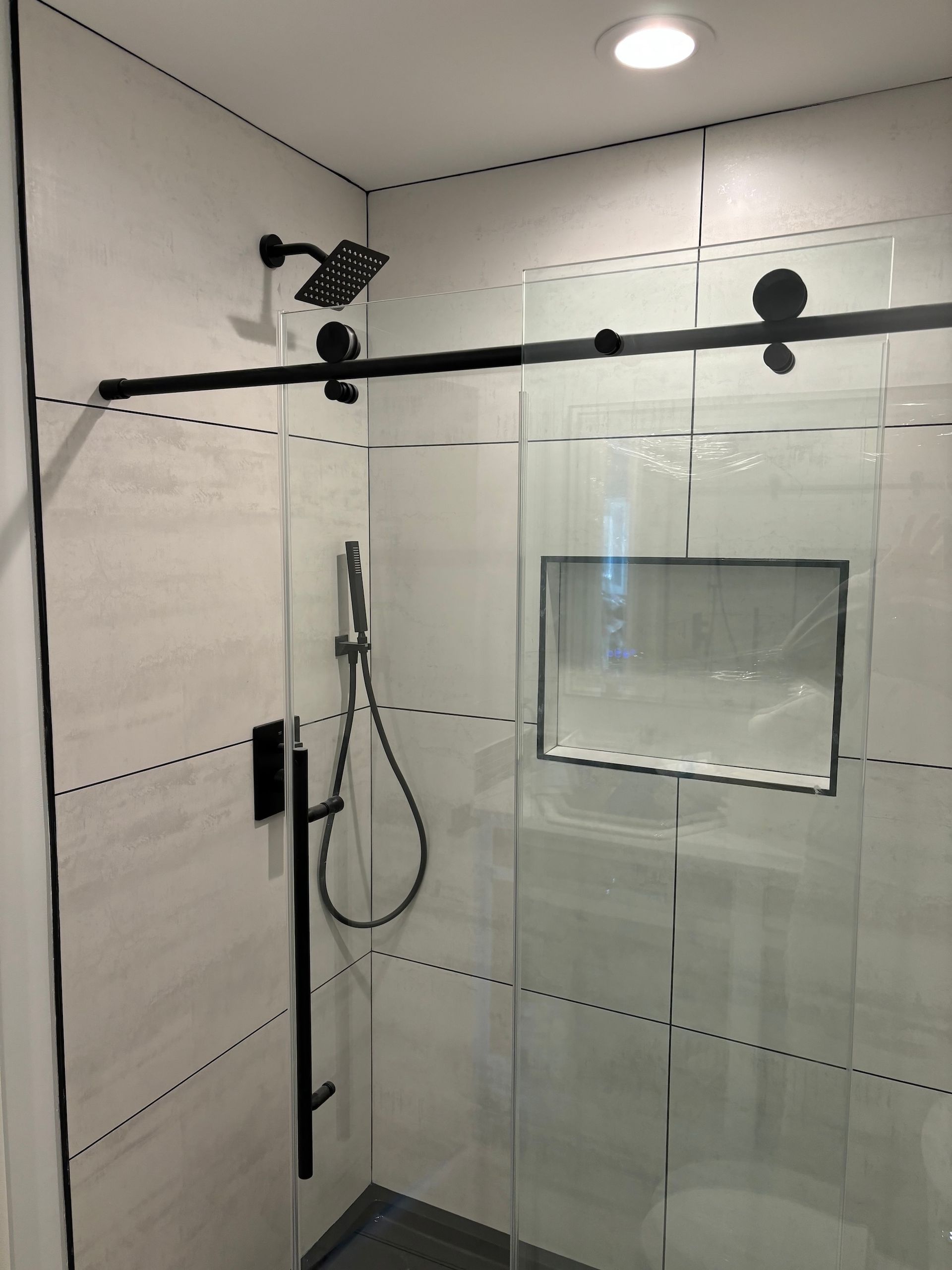 Black-framed glass shower enclosure with black fixtures and white tiled walls.