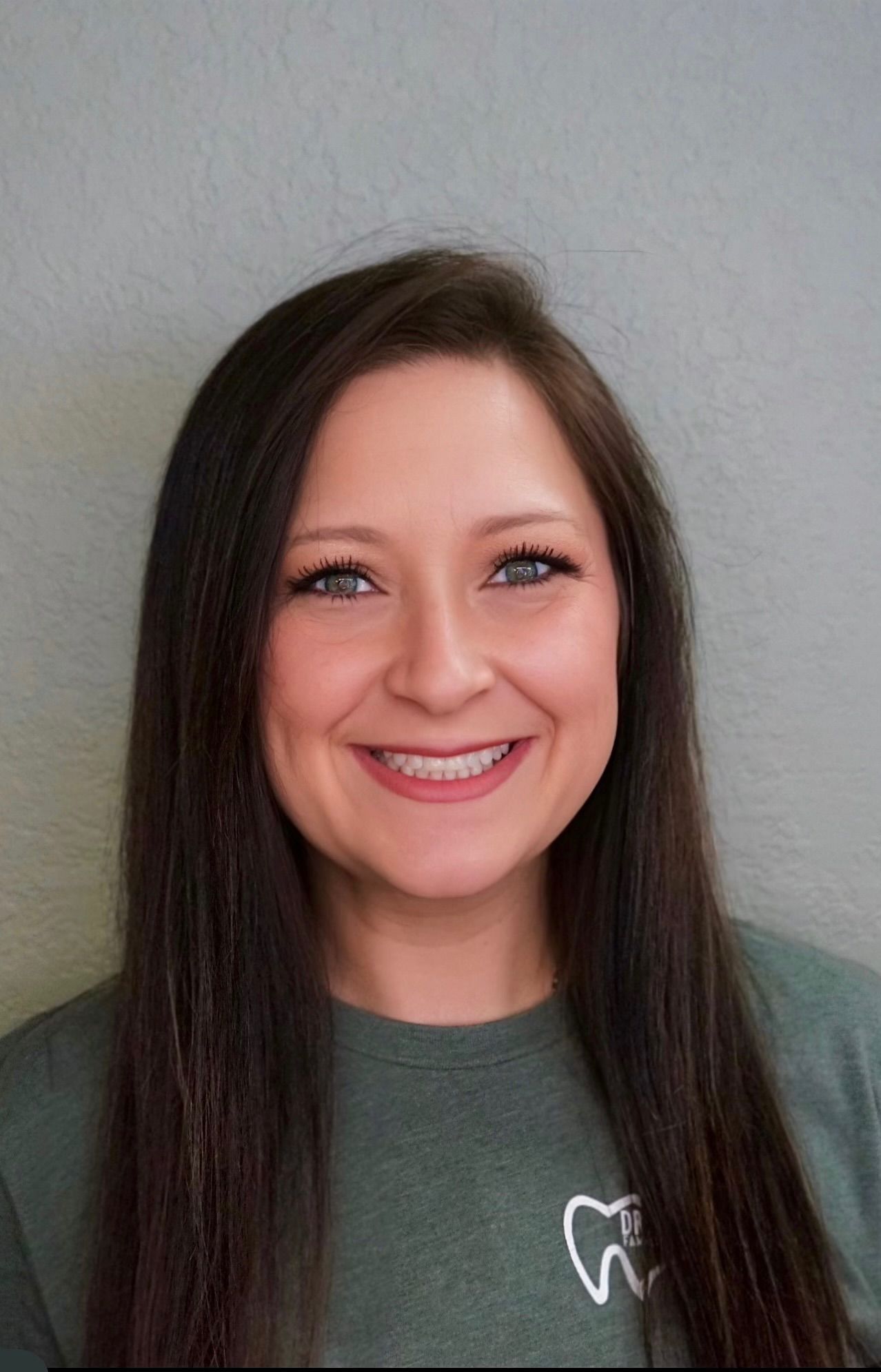 The woman is wearing a blue scrub top and smiling for the camera.