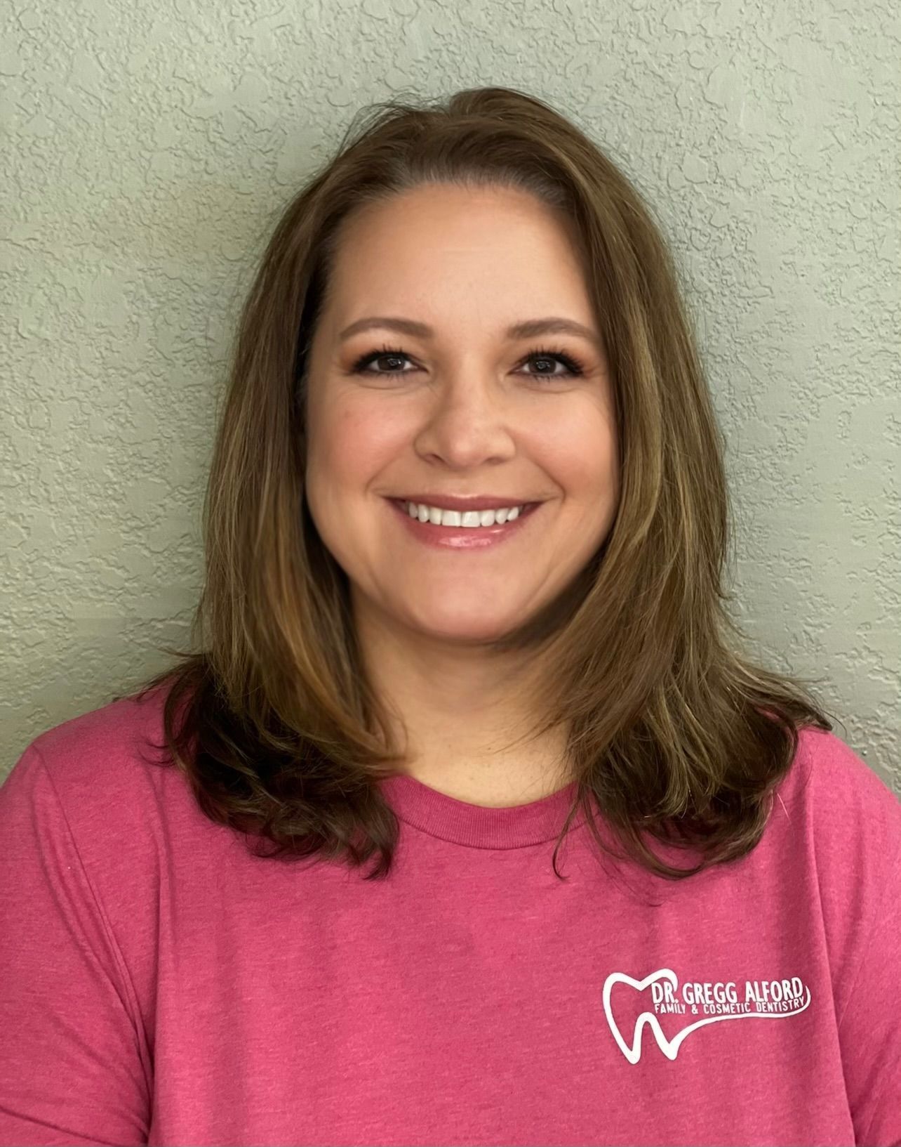 A woman is smiling for the camera and wearing a green shirt.