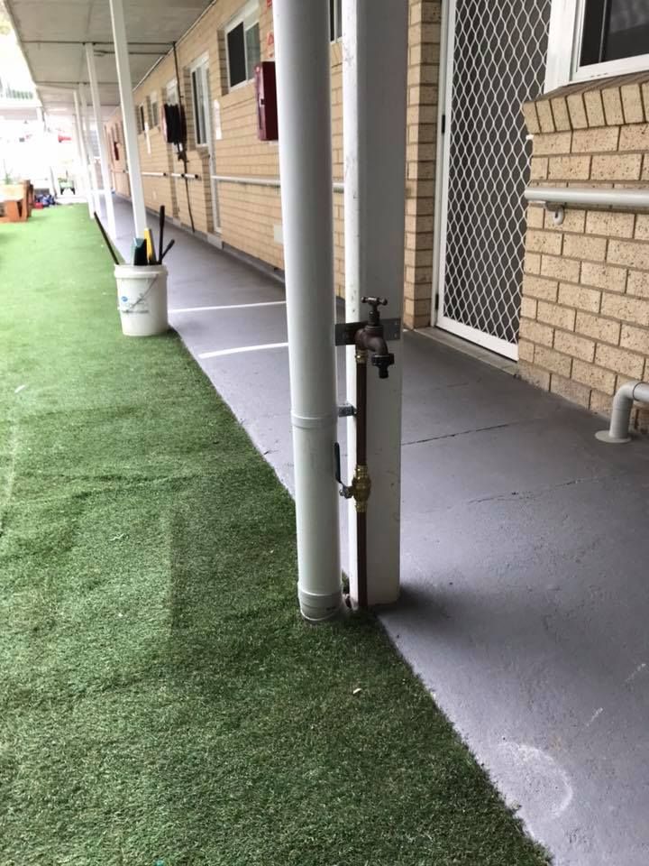 A Hose Is Attached To A Pole In A Hallway Next To A Brick Building — Richardson Plumbing & Gas Service In Port Macquarie, NSW