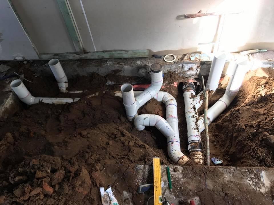 A Bunch Of Pipes Are Laying In The Dirt — Richardson Plumbing & Gas Service In Port Macquarie, NSW