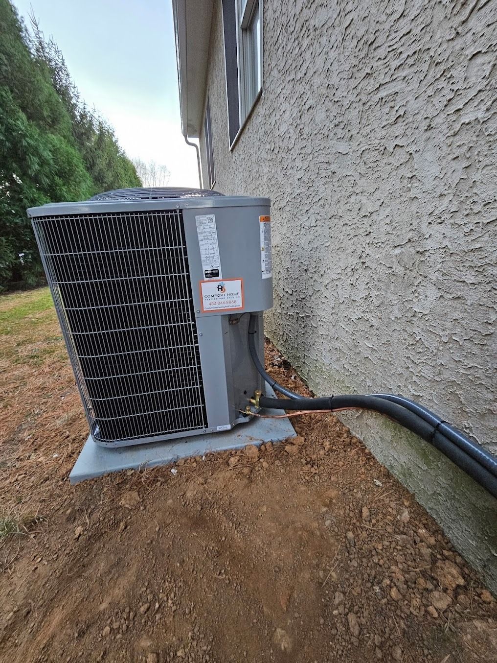 Air conditioner unit next to a stucco wall; brown dirt foreground; cloudy sky.