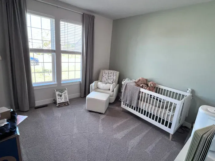 Baby nursery with white crib, rocking chair, and green accent wall.