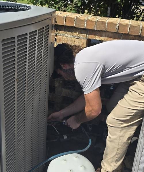 A man in a blue jacket is working on an air conditioner
