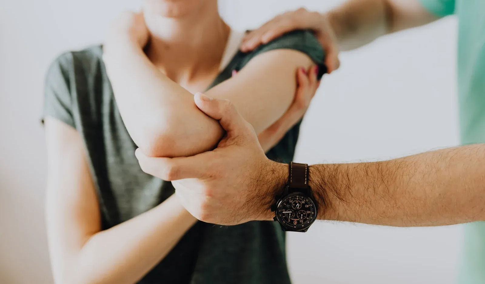 Person's elbow being examined by another person; white background, medical check-up.