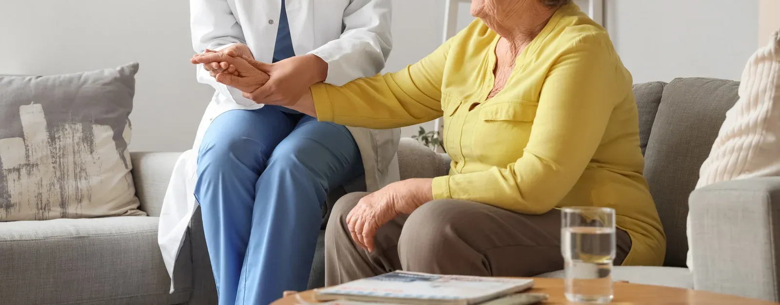 A healthcare professional examines a patient's arm while seated on a couch.