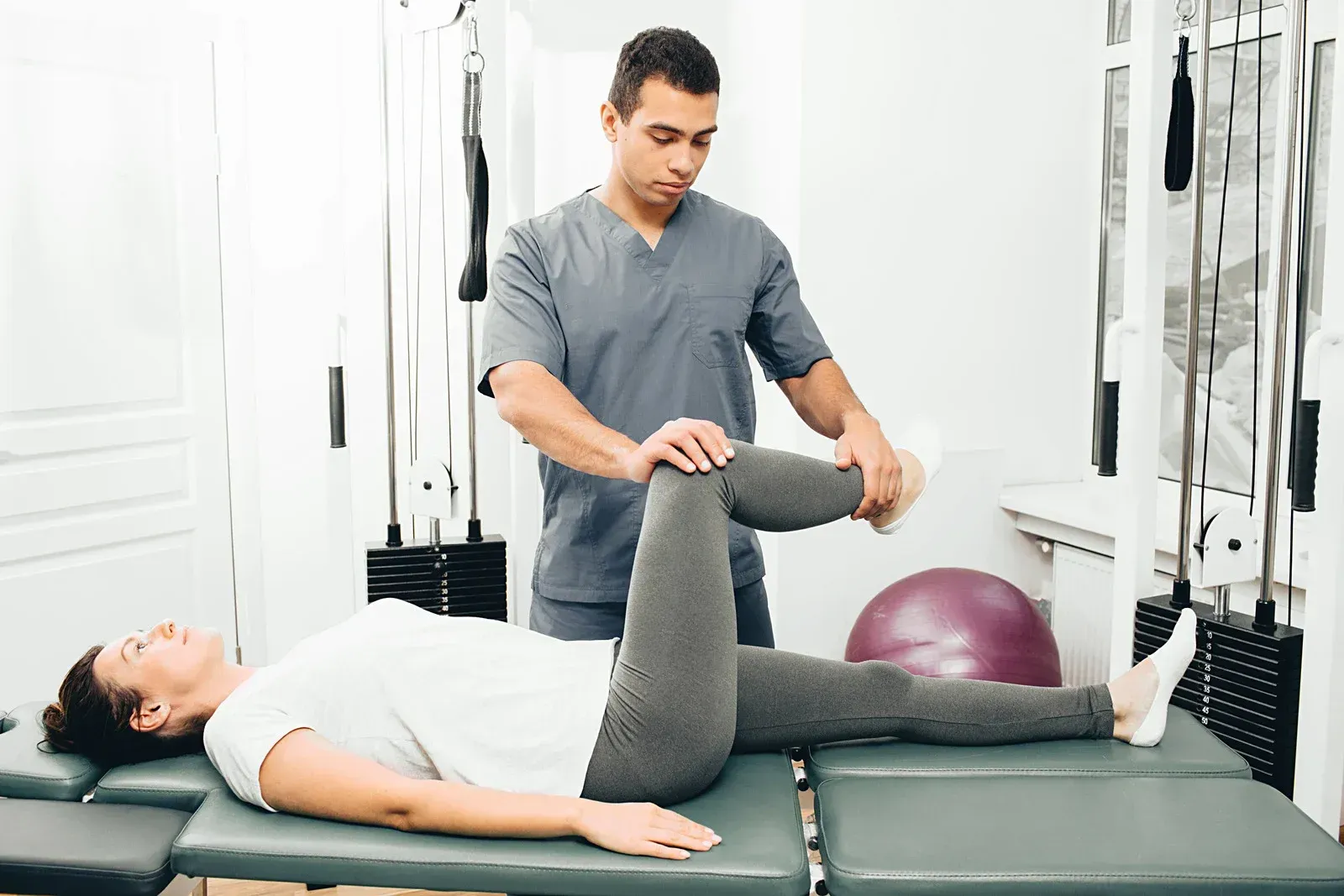Physical therapist assisting a person with a leg exercise in a therapy room.