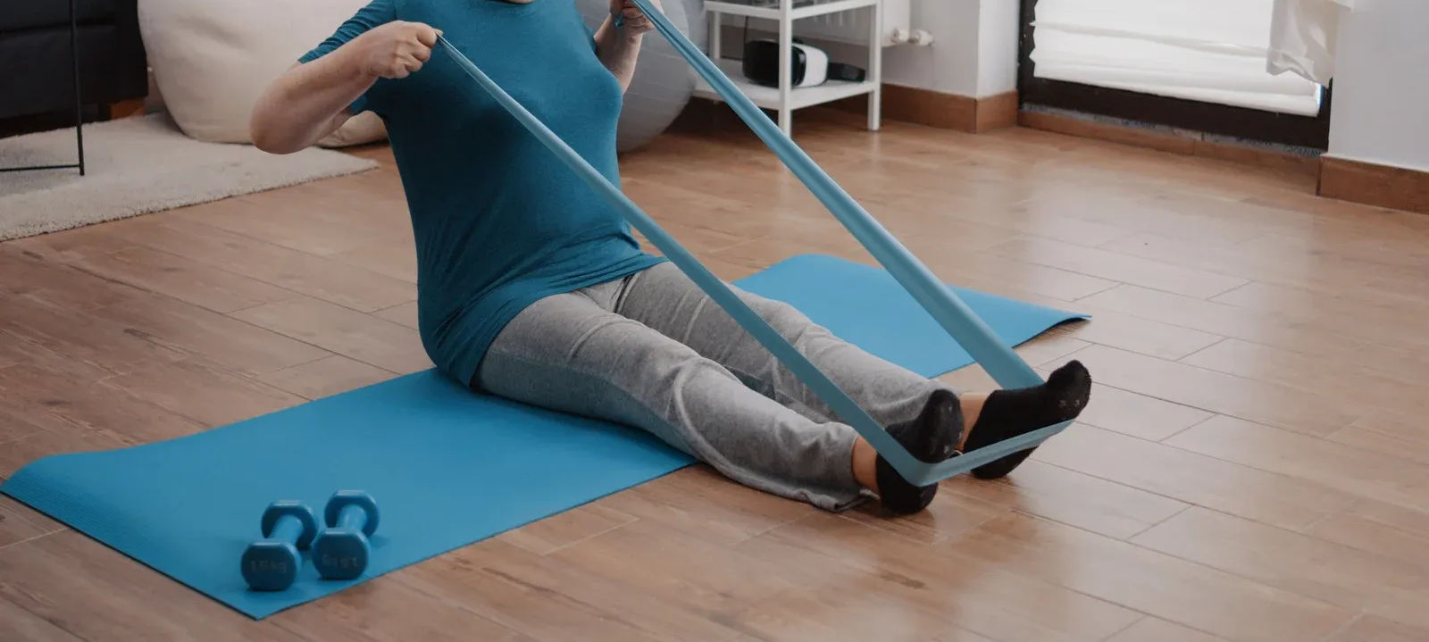 Person seated on a blue mat, using a resistance band for exercise.