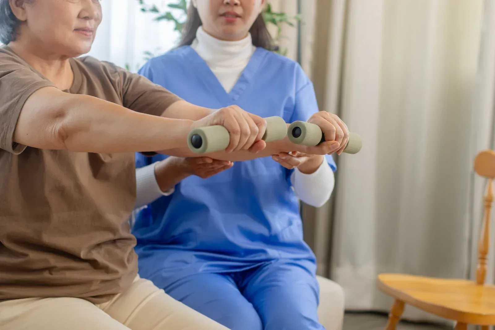 Therapist assists a person exercising with a dumbbell in a room.