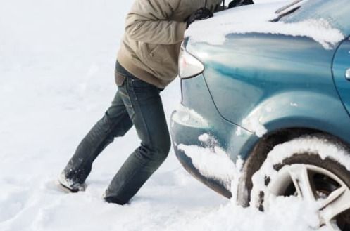 Man pushing a blue car stuck in deep snow. Winter scene.