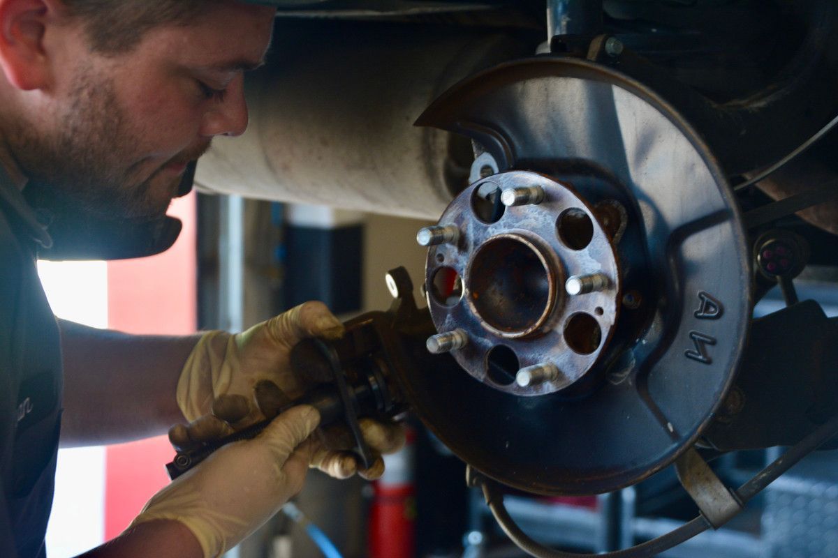 Mechanic replacing brake rotor on a car in a garage; wearing gloves.