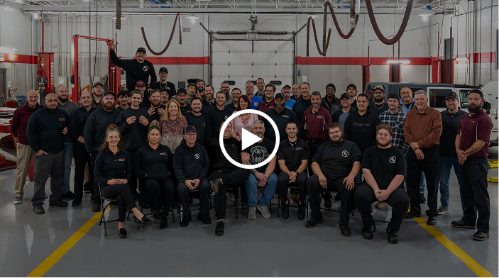 A large group of people are posing for a picture in a garage | Paul Campanella's Auto Centers