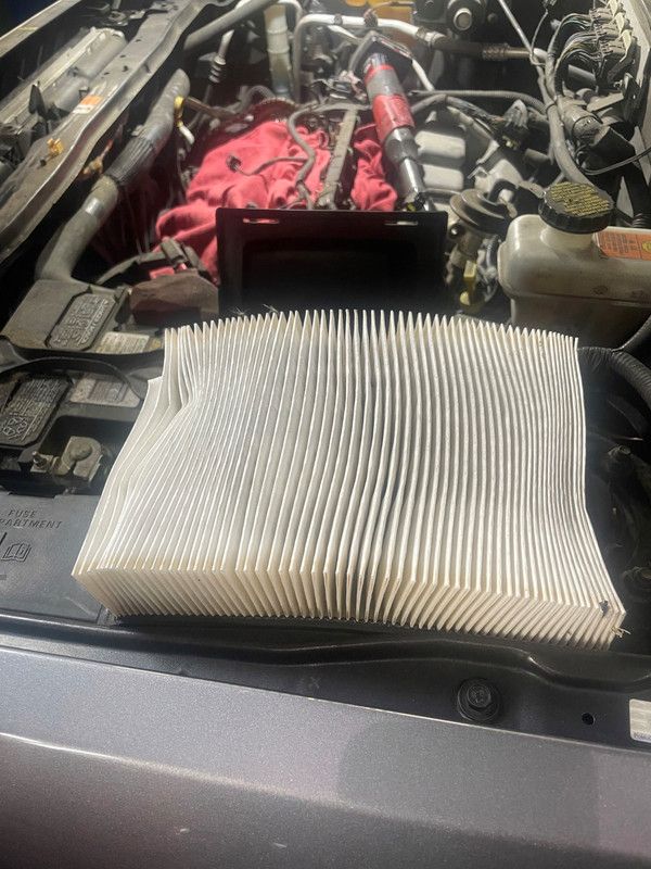 An old air filter sits on top of a car engine, ready to be replaced.
